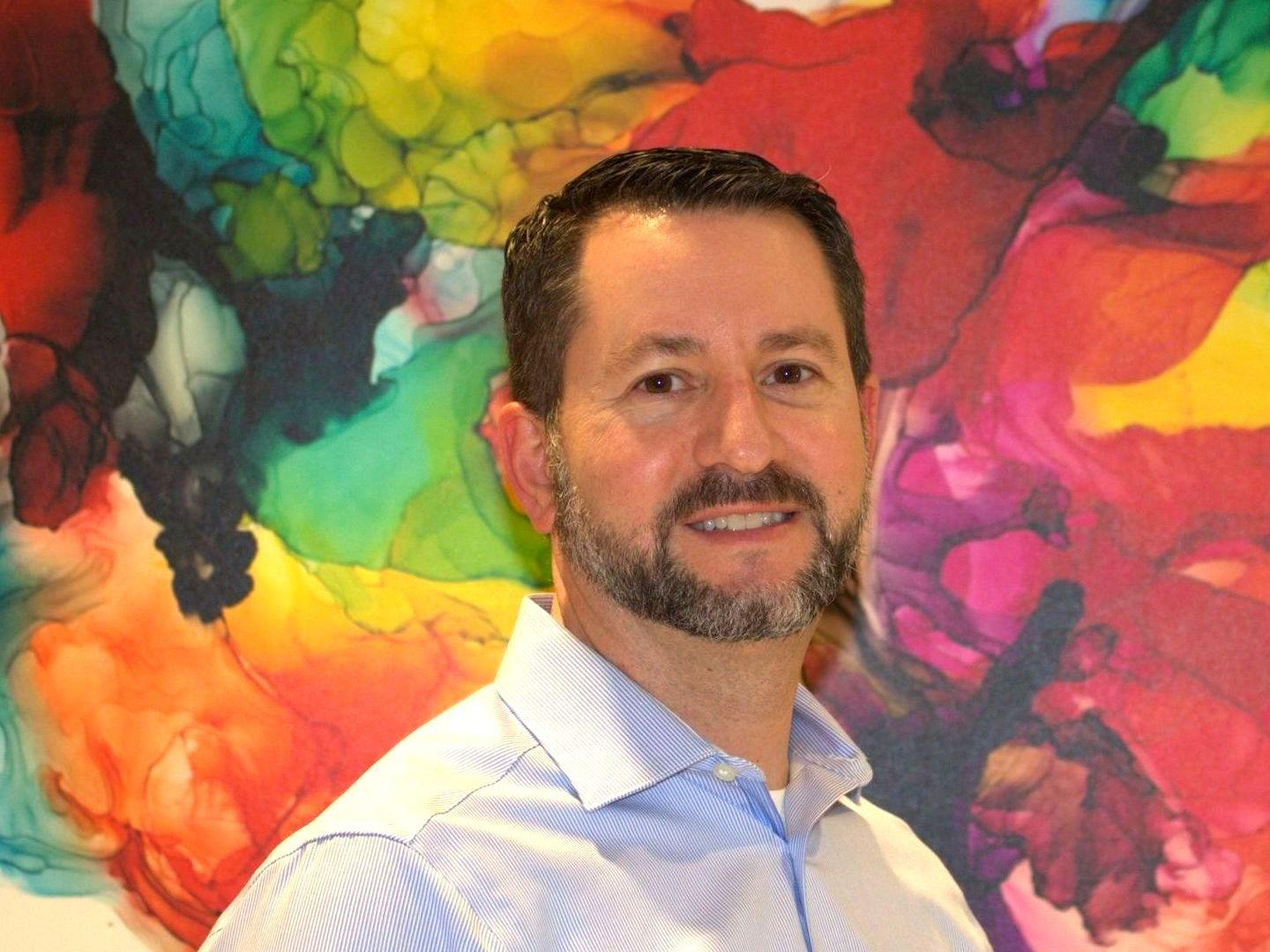 Dr. Budman is smiling in front of a colorful painting.