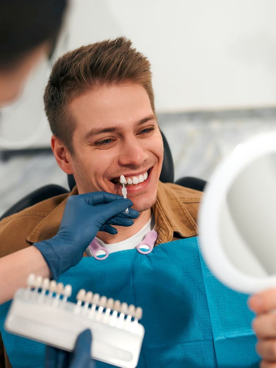 A man is sitting in a dental chair looking at his teeth in a mirror.