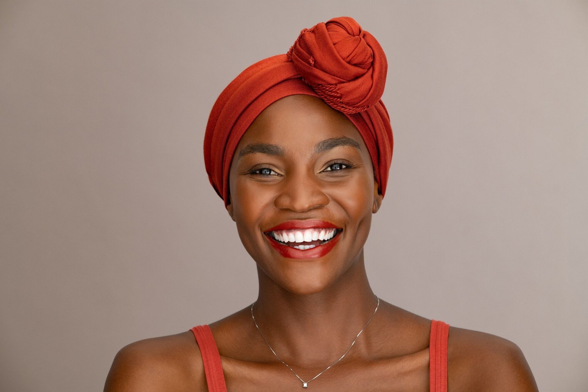 A woman wearing a red turban and red lipstick is smiling.