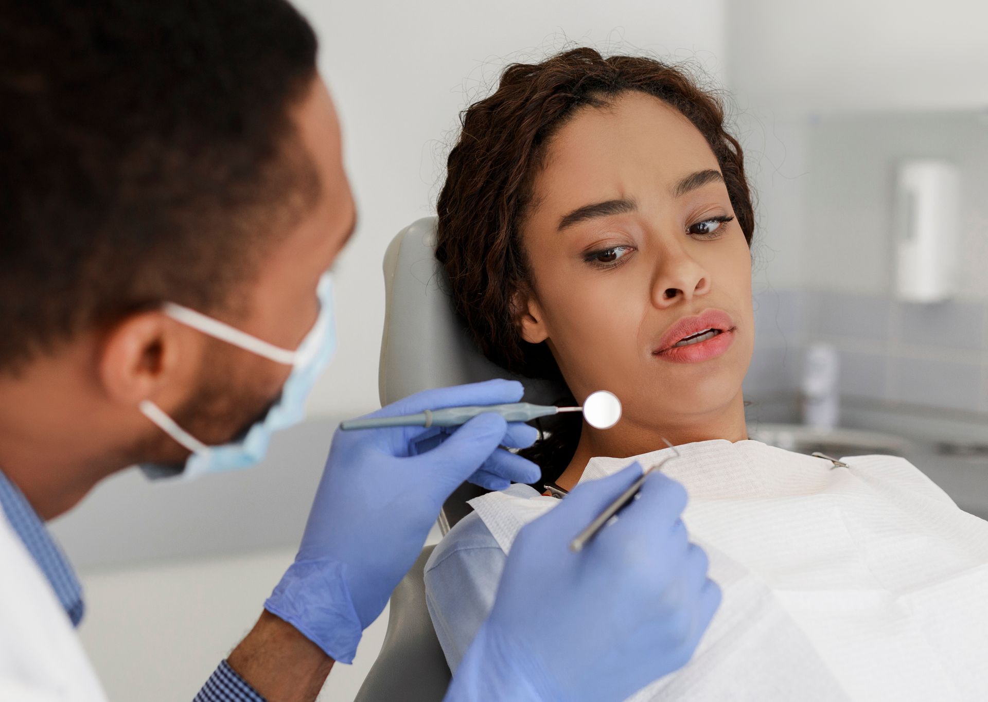 Dentist examining a patient’s mouth with a dental mirror and tool, wearing gloves and a mask.