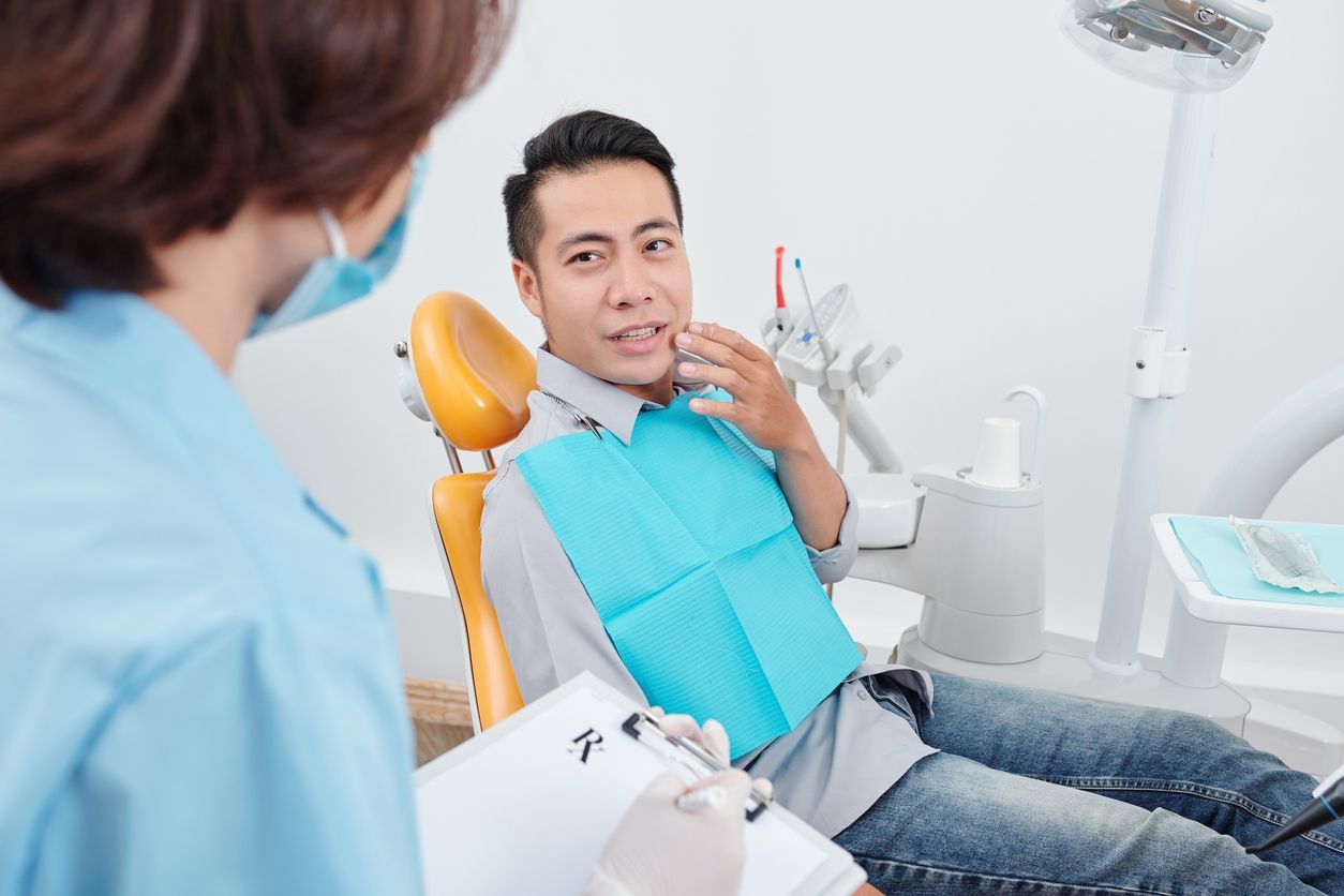 A man is sitting in a dental chair talking to a dentist.