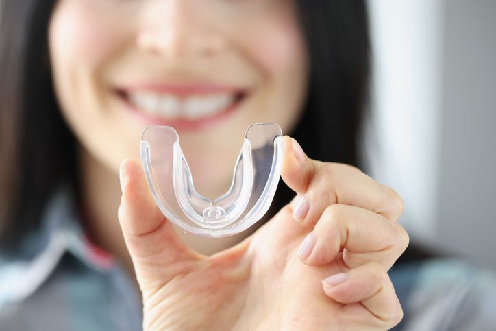 Hand holding a clear dental aligner in front of a smiling face