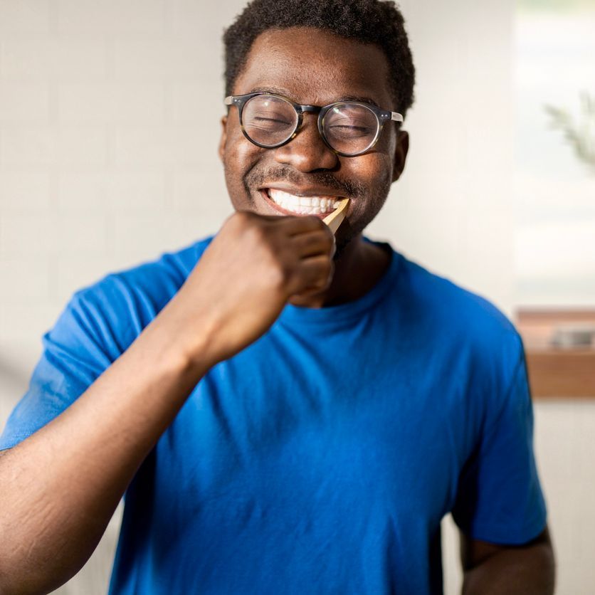 A man wearing glasses and a blue shirt is brushing his teeth.
