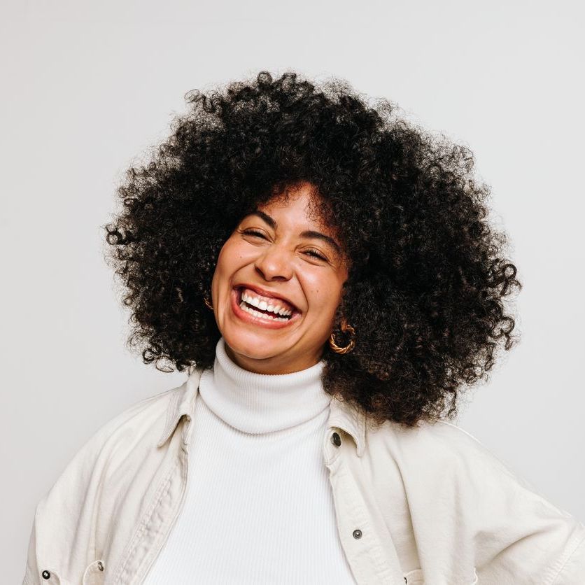 A woman with curly hair is smiling and wearing a white shirt.