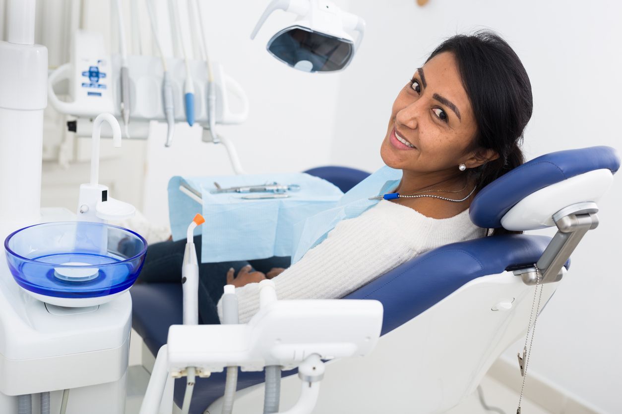 A woman is sitting in a dental chair and smiling.