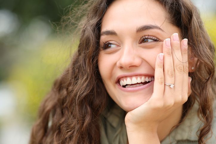 Smiling woman with curly hair resting her face on her hand outdoors