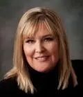 Blonde woman with bangs smiling, wearing a black turtleneck, studio shot.