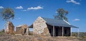 An old stone house with a porch in the middle of a field.