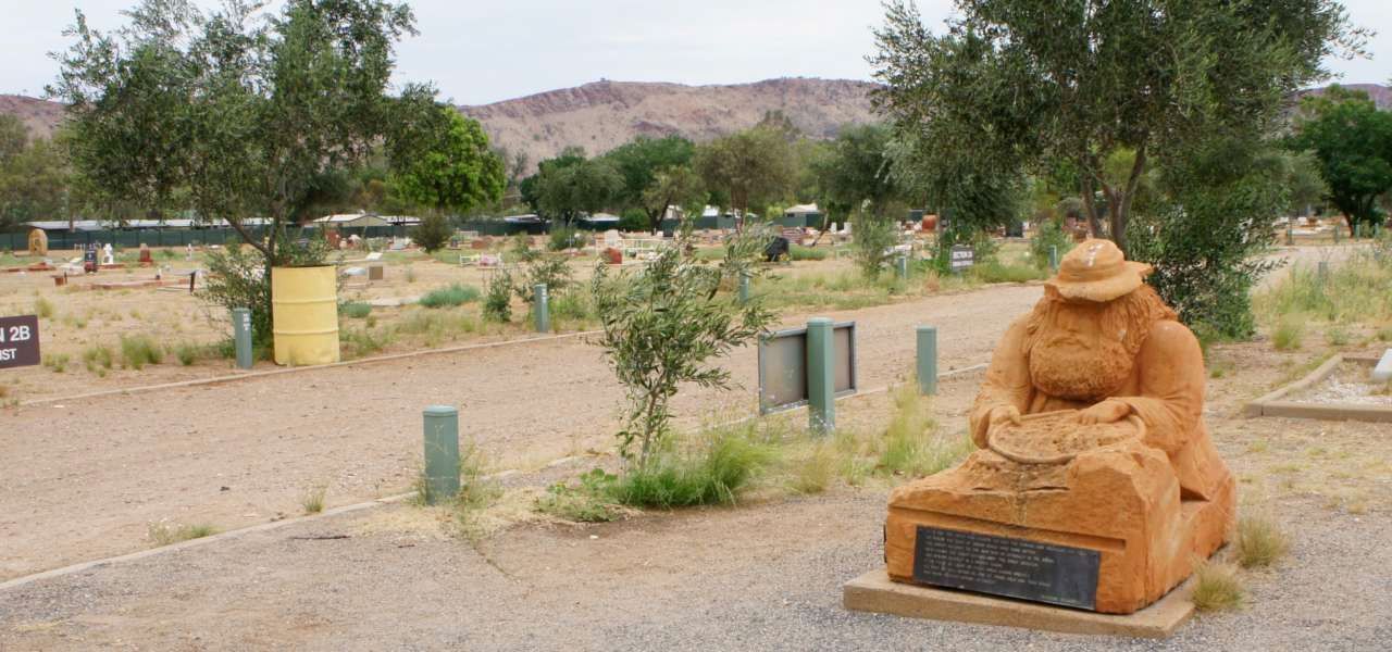 A statue of a man in a hat is sitting in the middle of a field.