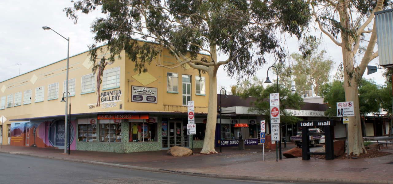 A yellow building is sitting on the corner of a street next to a tree.