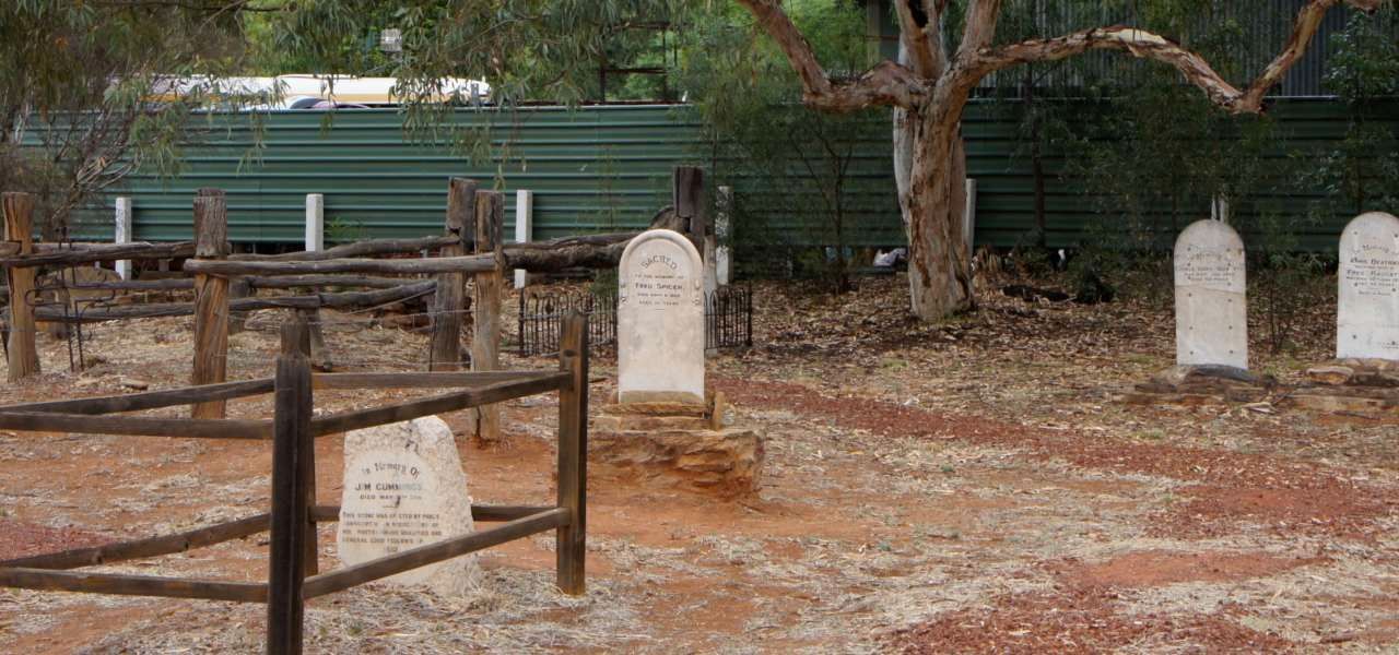 A cemetery with a wooden fence and graves in the dirt.