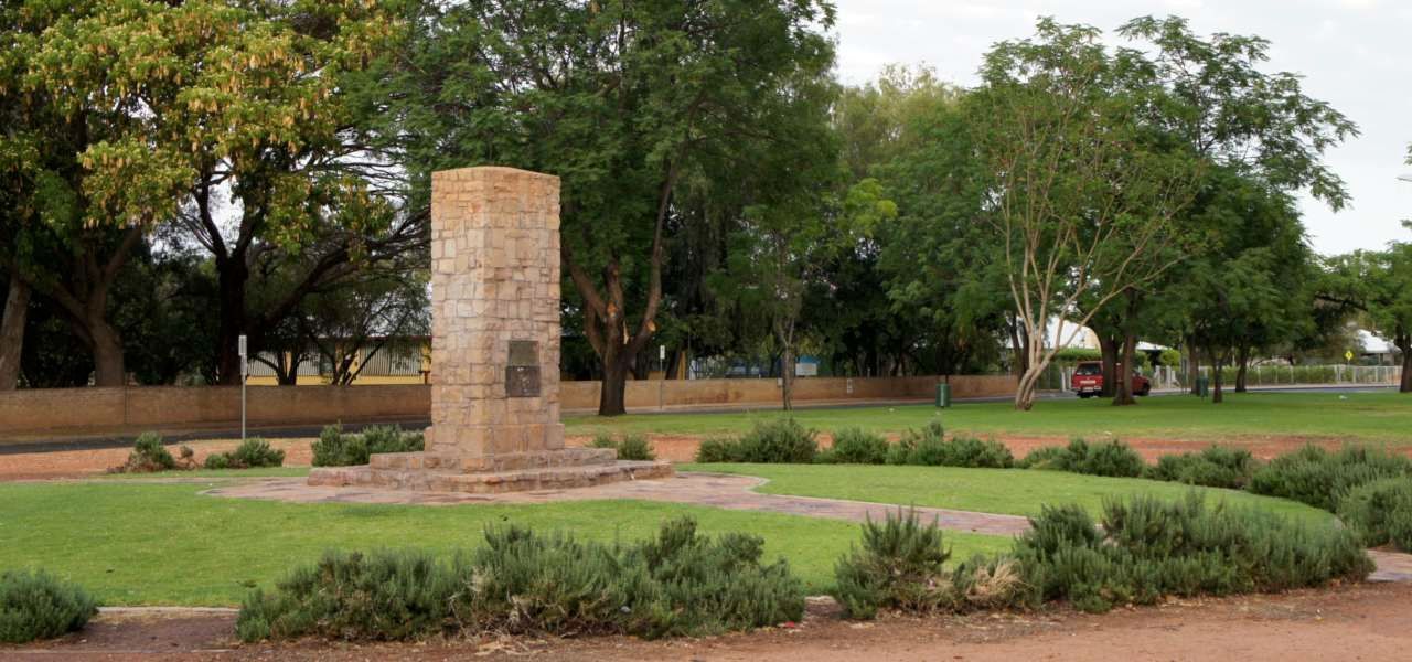 There is a statue in the middle of a park surrounded by trees.