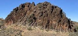 A large rock formation in the desert with a blue sky in the background.