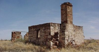 An old stone building with a chimney in the middle of a field.