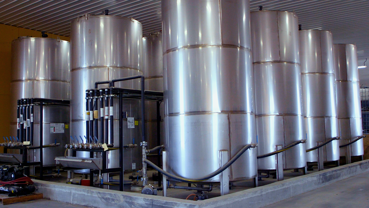 A row of large, cylindrical stainless steel industrial storage tanks in a warehouse setting.