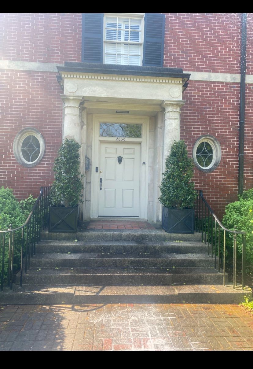 Brick house entrance with white door, steps, and potted topiary shrubs
