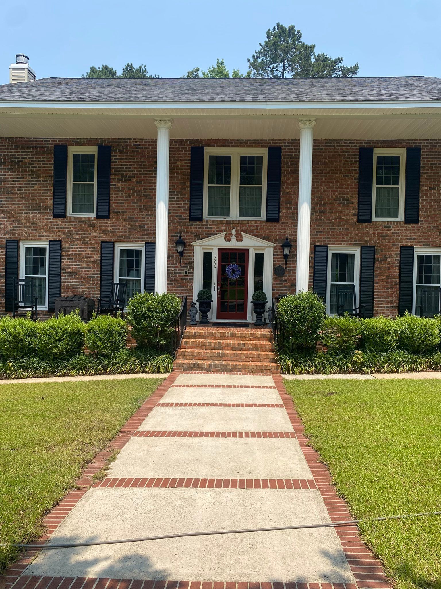 Brick colonial house with white columns, black shutters, and a red-brick walkway leading to the front door