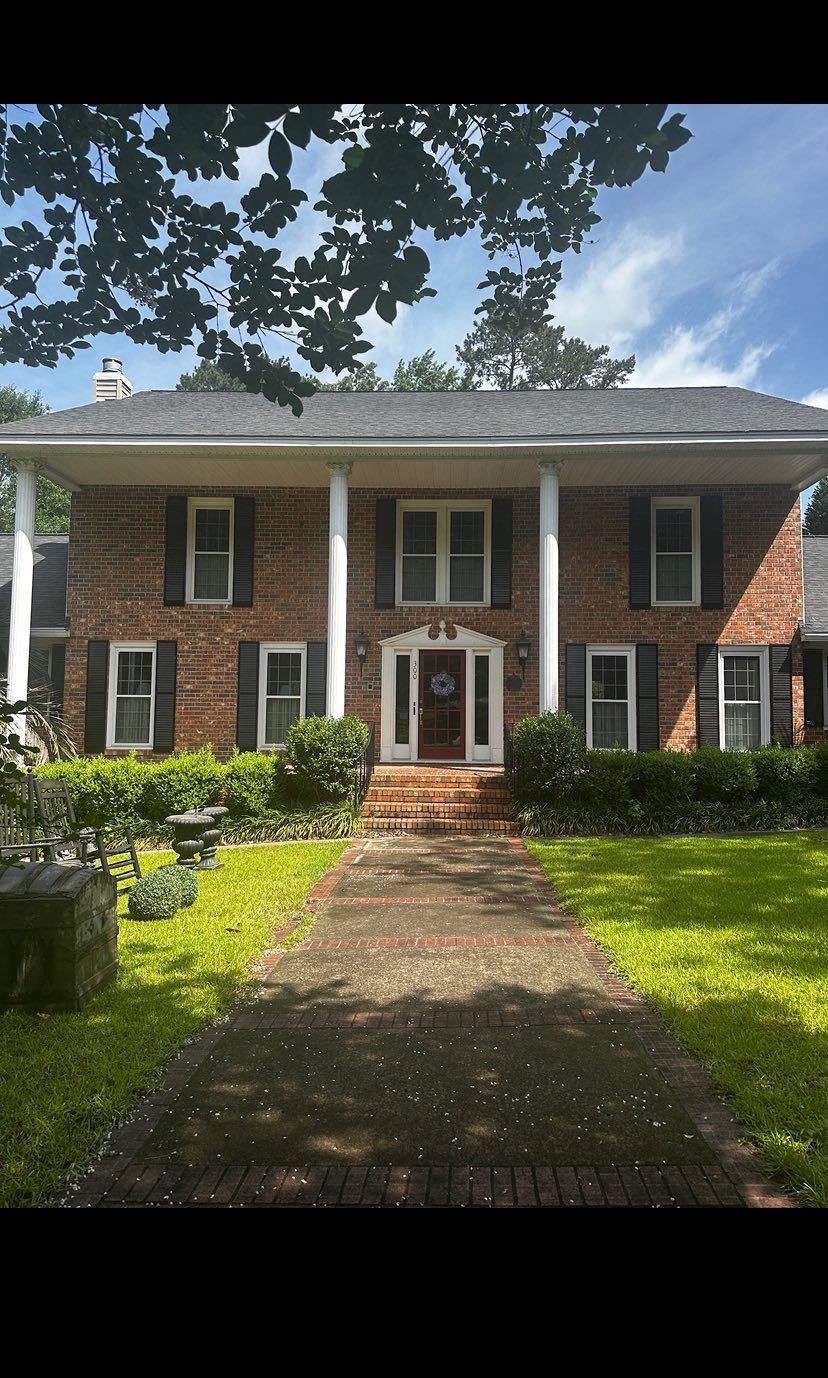 Brick two-story house with white columns, front brick walkway, and green lawn under a leafy tree.