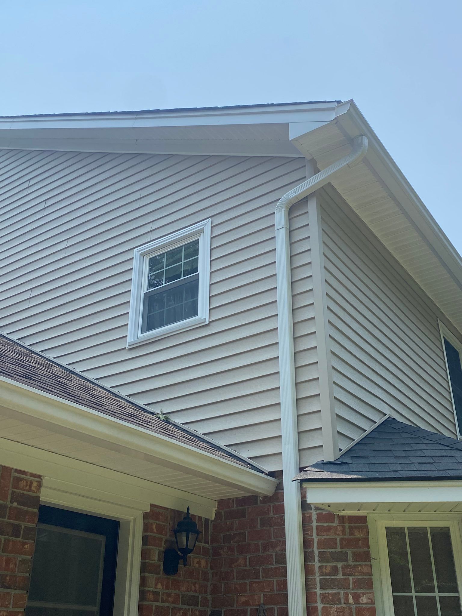 Exterior of a suburban house with beige siding, brick walls, and a second-story window under a blue sky