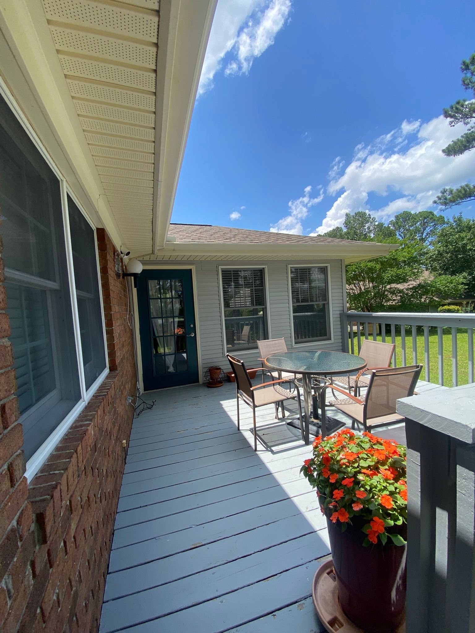 Front porch patio with table, chairs, potted flowers, and blue sky on a sunny day
