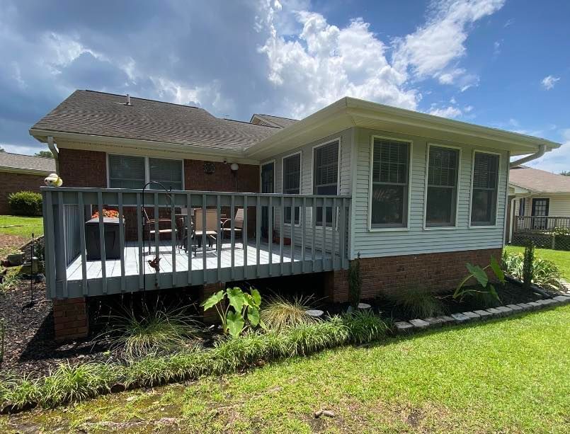 Suburban house with a white-railed front deck, brick base, and green lawn under a cloudy sky