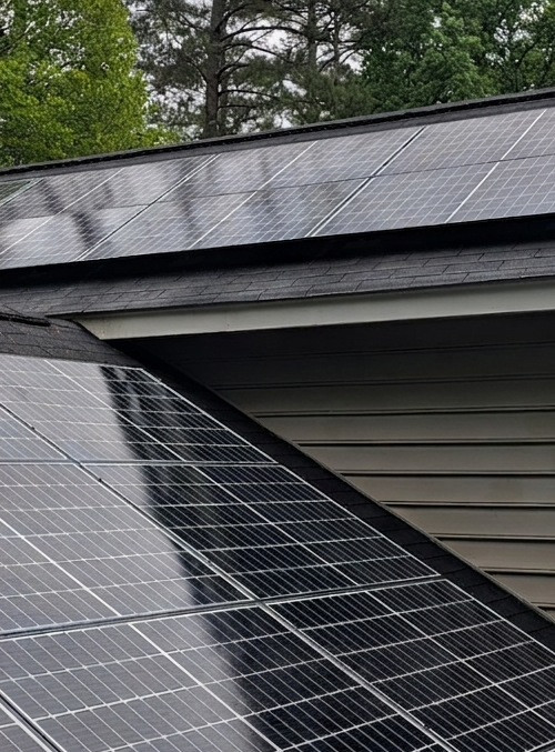 Solar panels on a house roof beneath trees, with one panel partially detached at the edge.