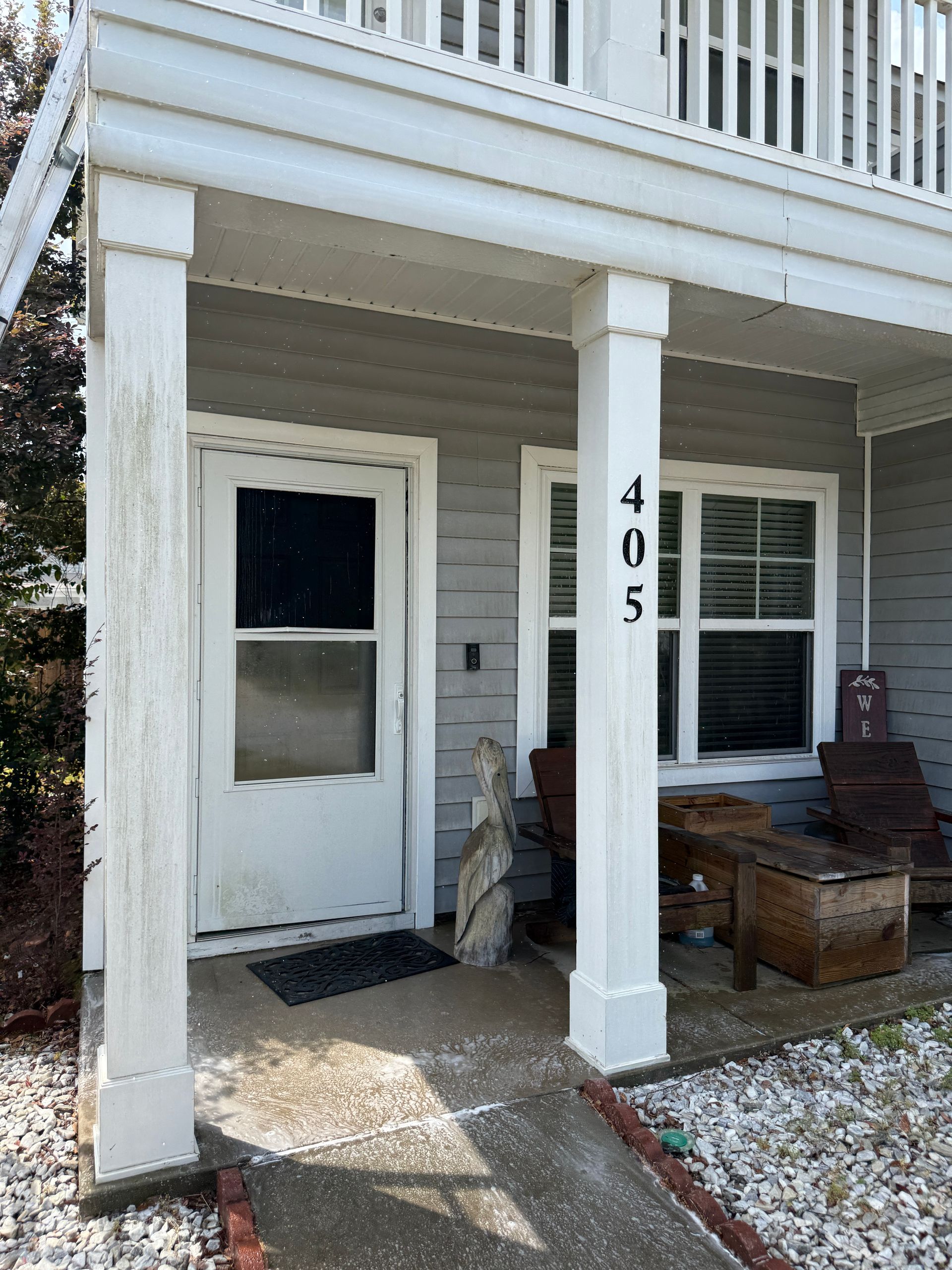 Front porch of a white house with a column, numbered 205, a door, and outdoor chairs.