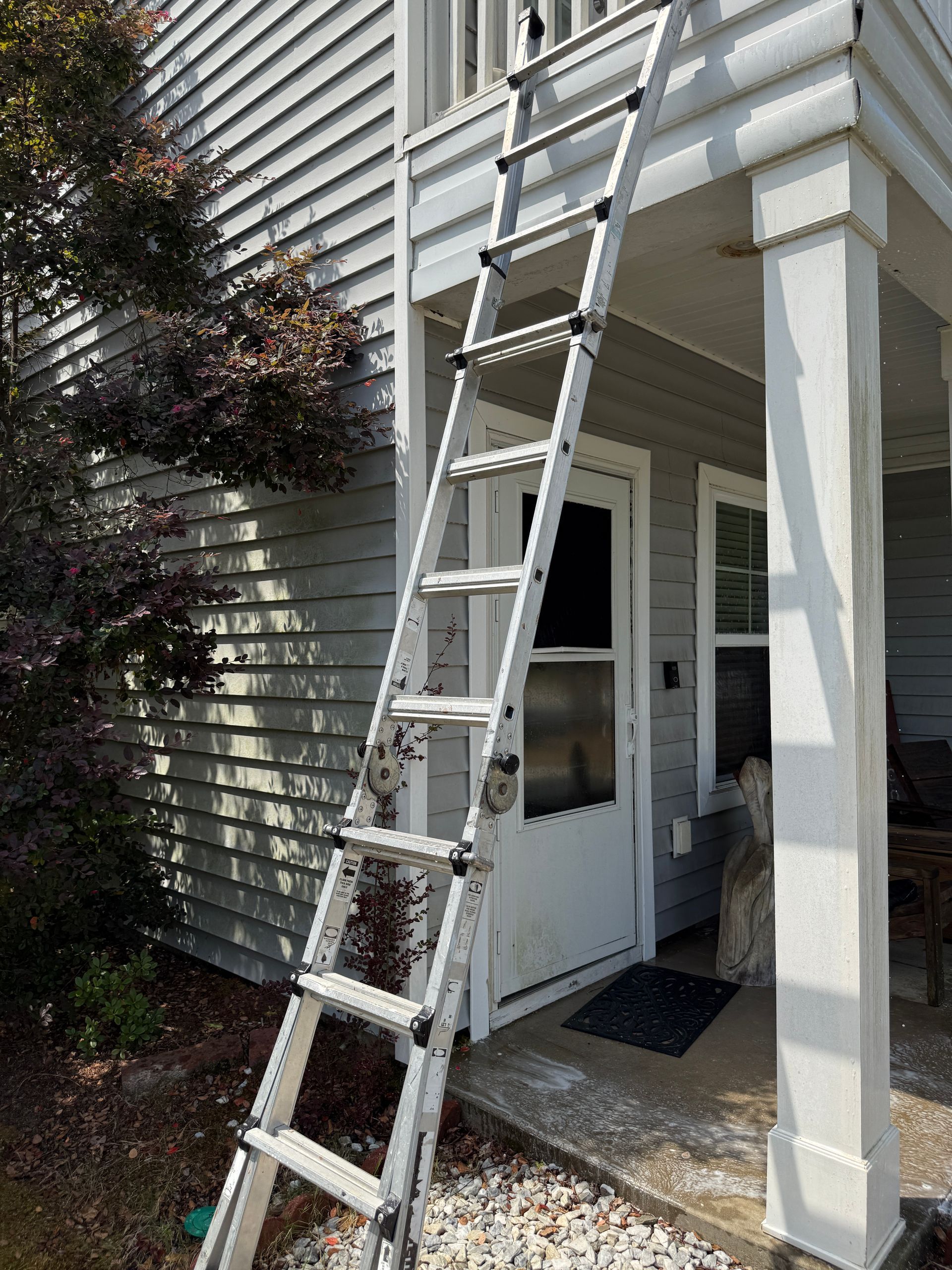 Aluminum extension ladder leaning against a house above a front porch with white columns