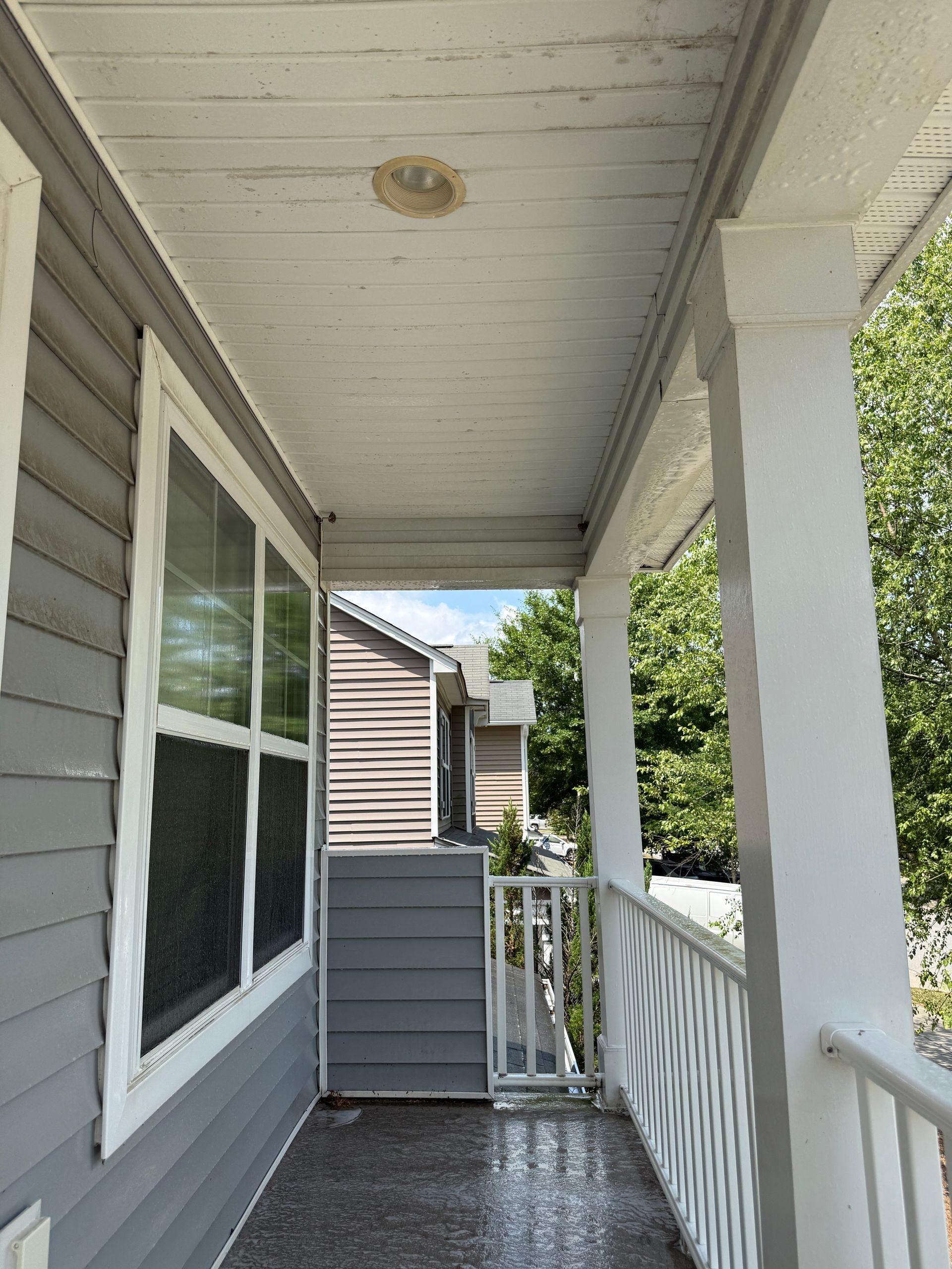 Covered front porch with white railing, gray siding, window, and ceiling light.