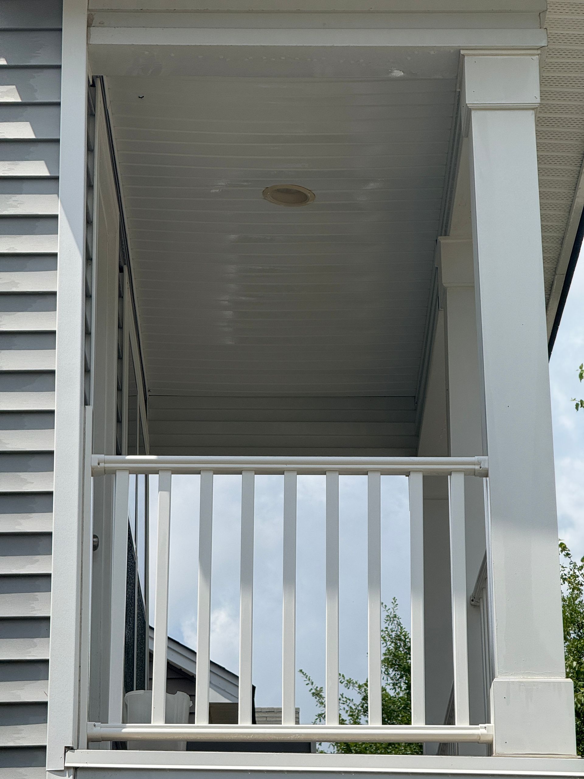 Front porch with white railing and columns under a covered ceiling.