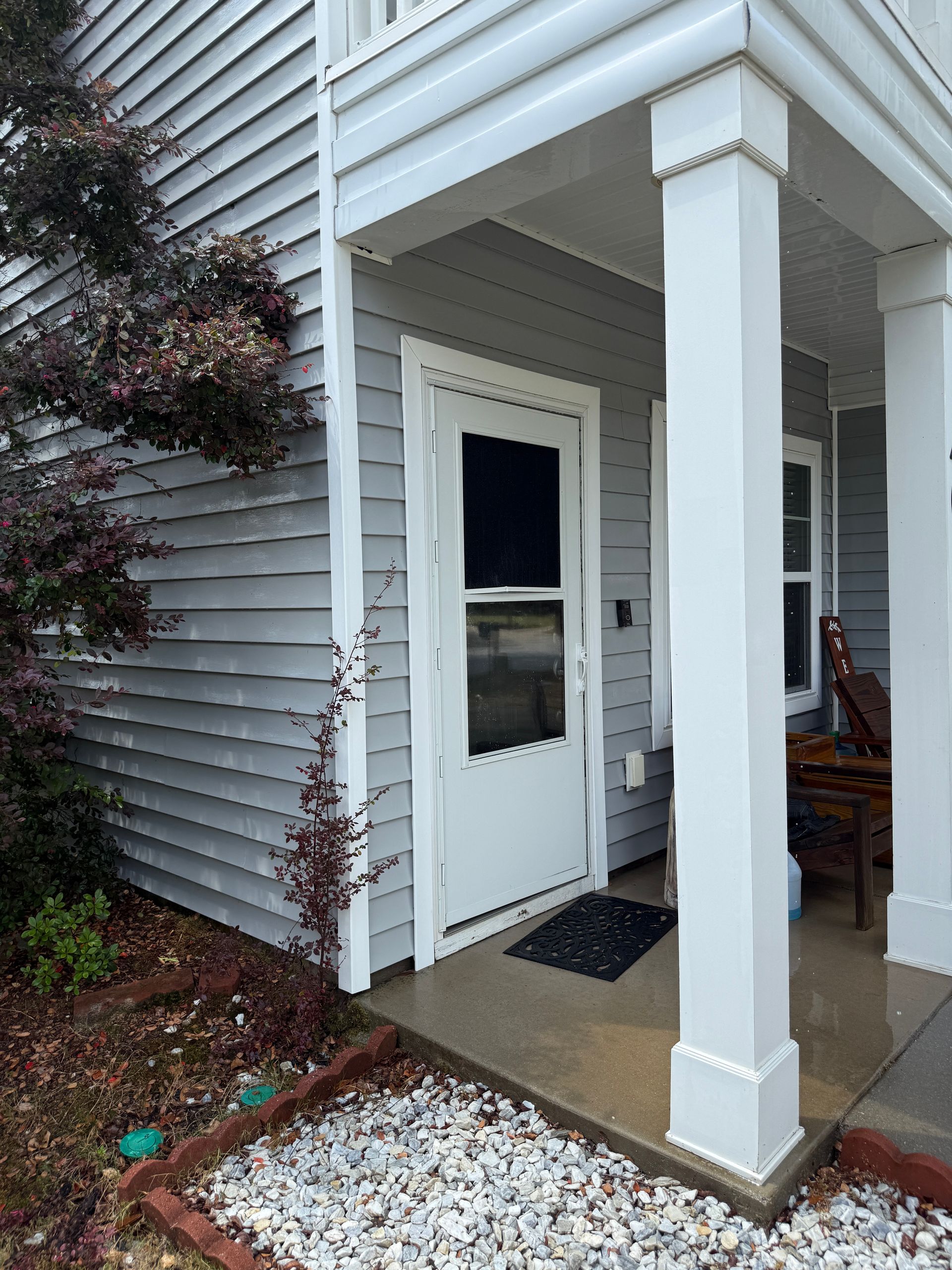 Covered front porch with white columns, gray siding, and a white door with a small window.