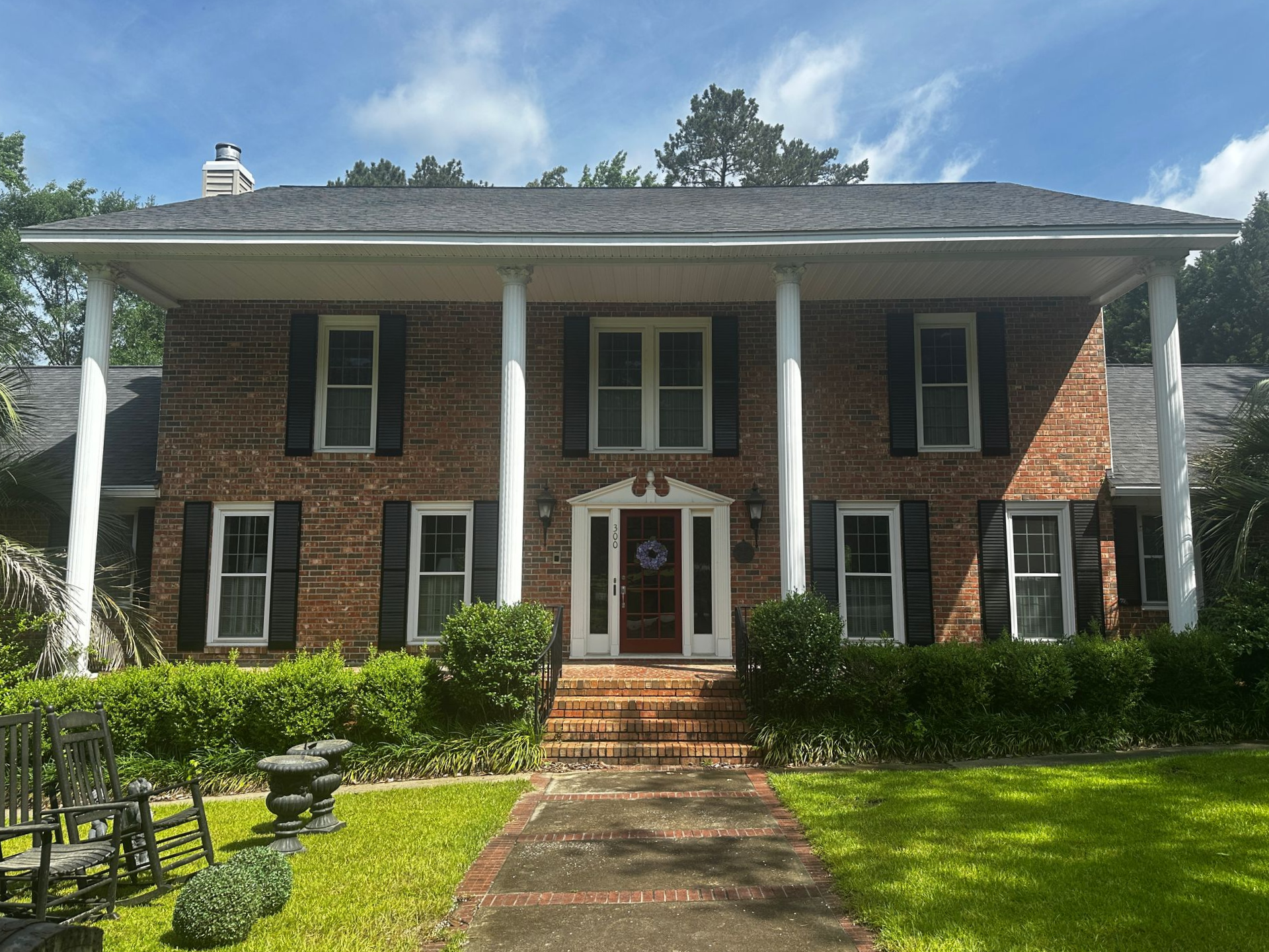 Two-story brick house with white columns and a red-brick walkway leading to the front door.