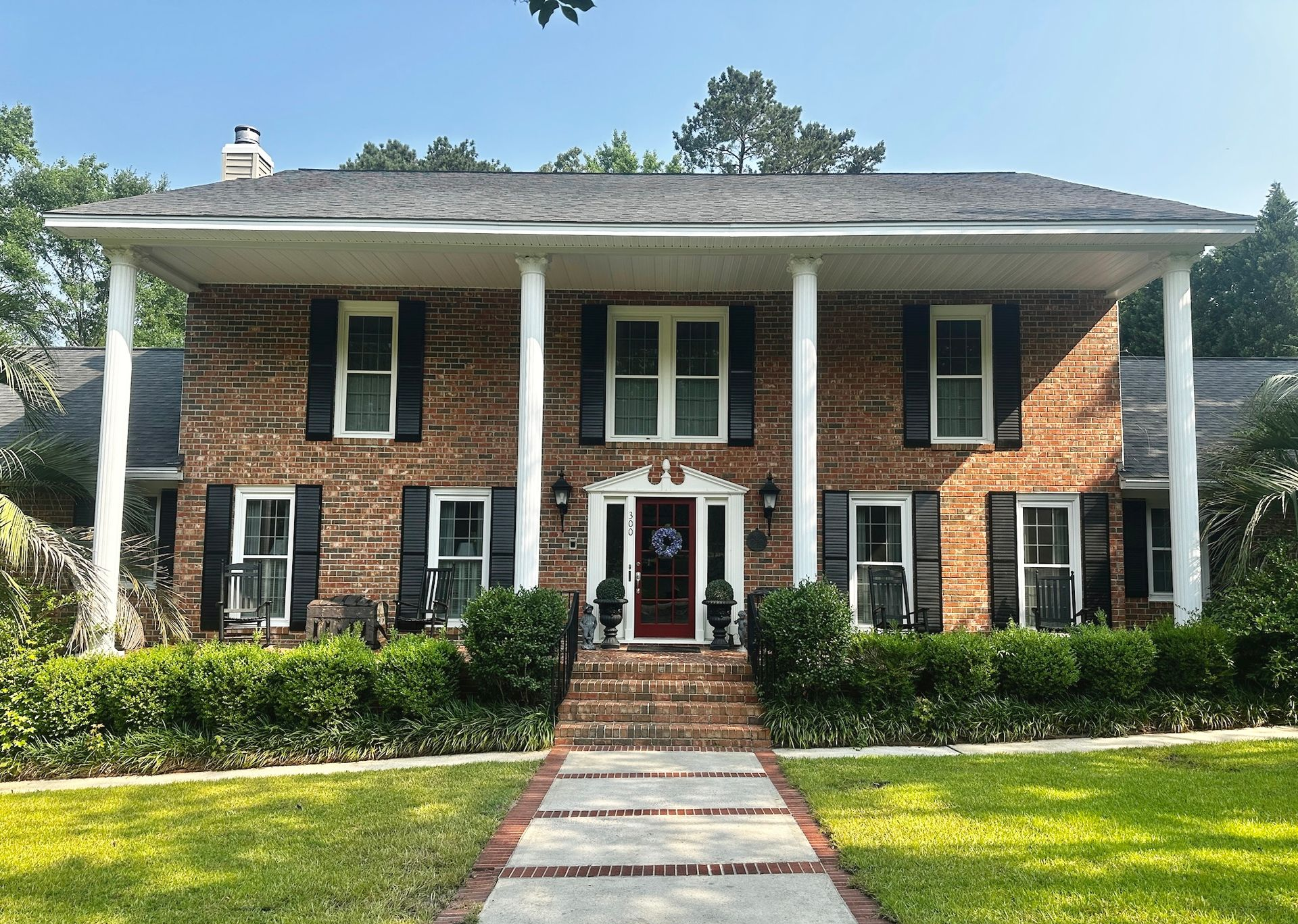 Brick two-story house with white columns, front walkway, and green lawn under leafy trees