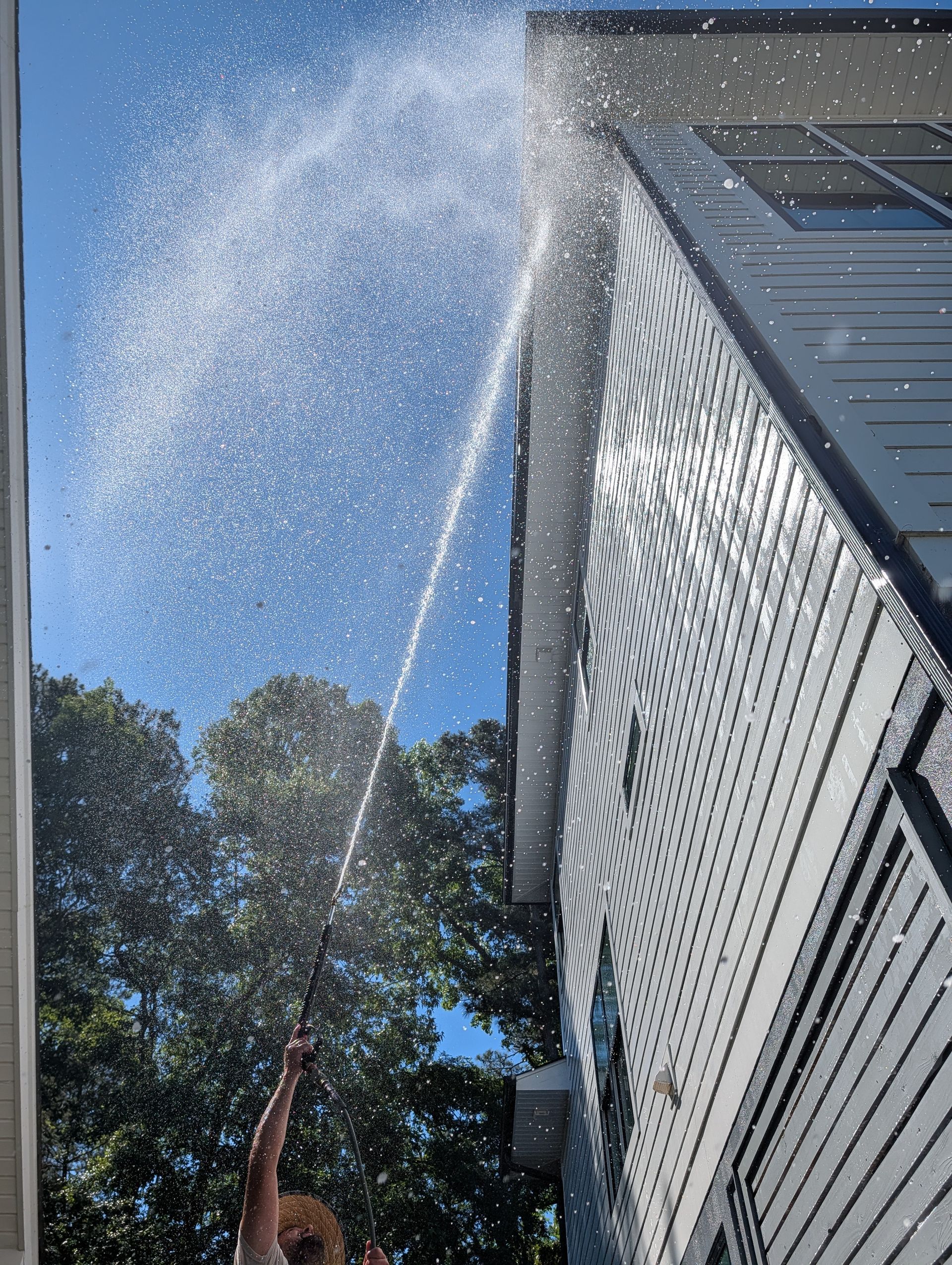 Person spraying water high into the air beside a tall house on a sunny day