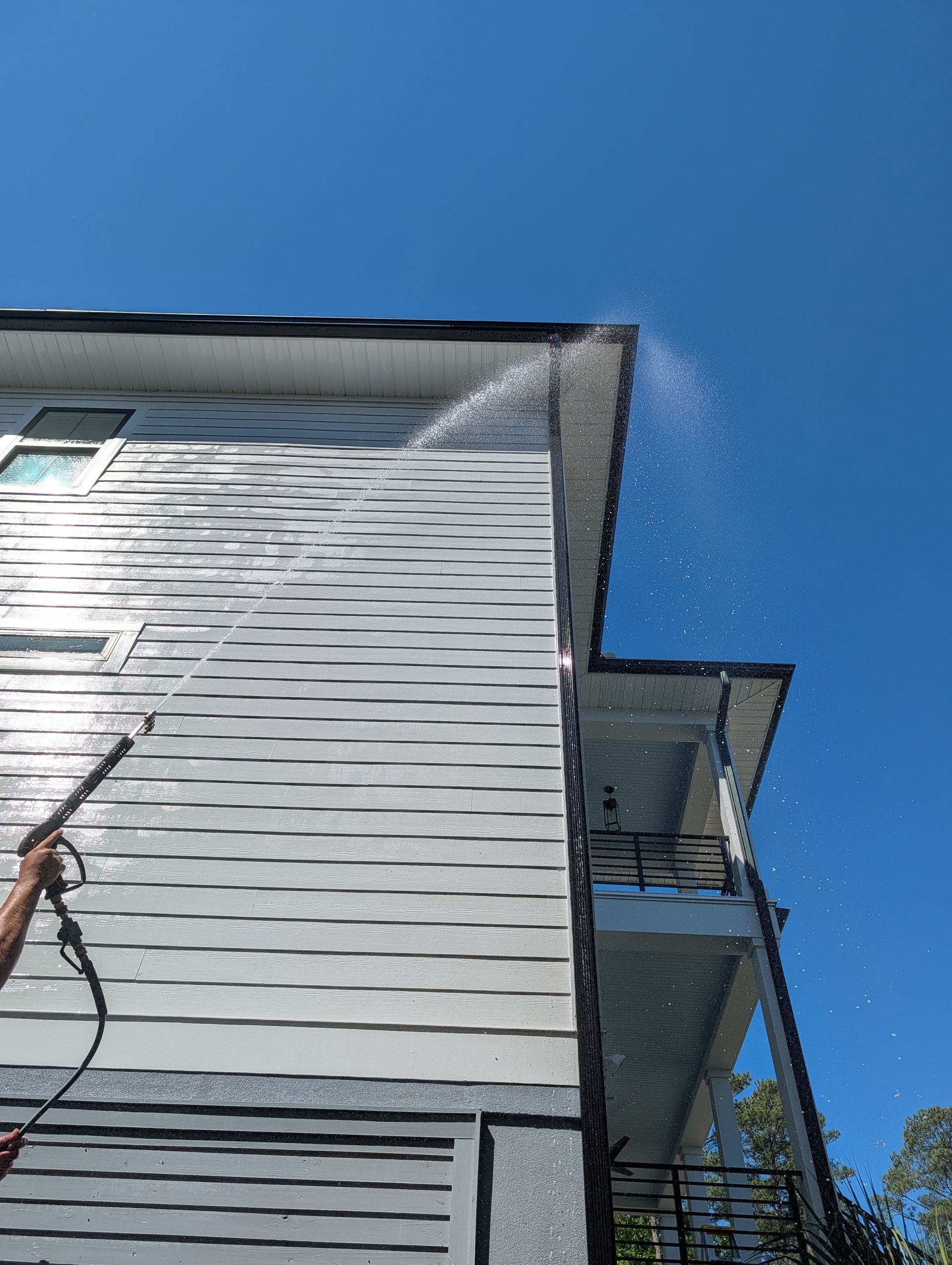 Low-angle view of a gray house exterior with balconies against a bright blue sky