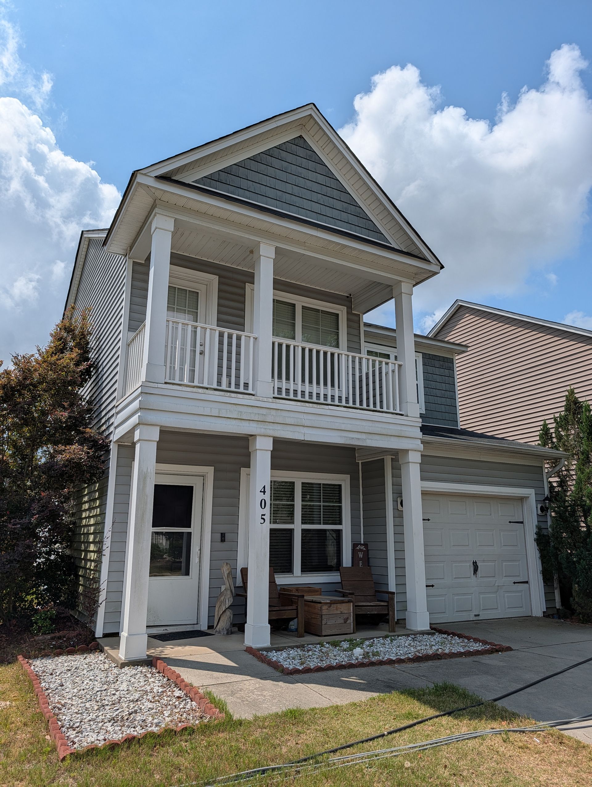 Two-story white house with a front porch, balcony, and brick driveway under a partly cloudy sky