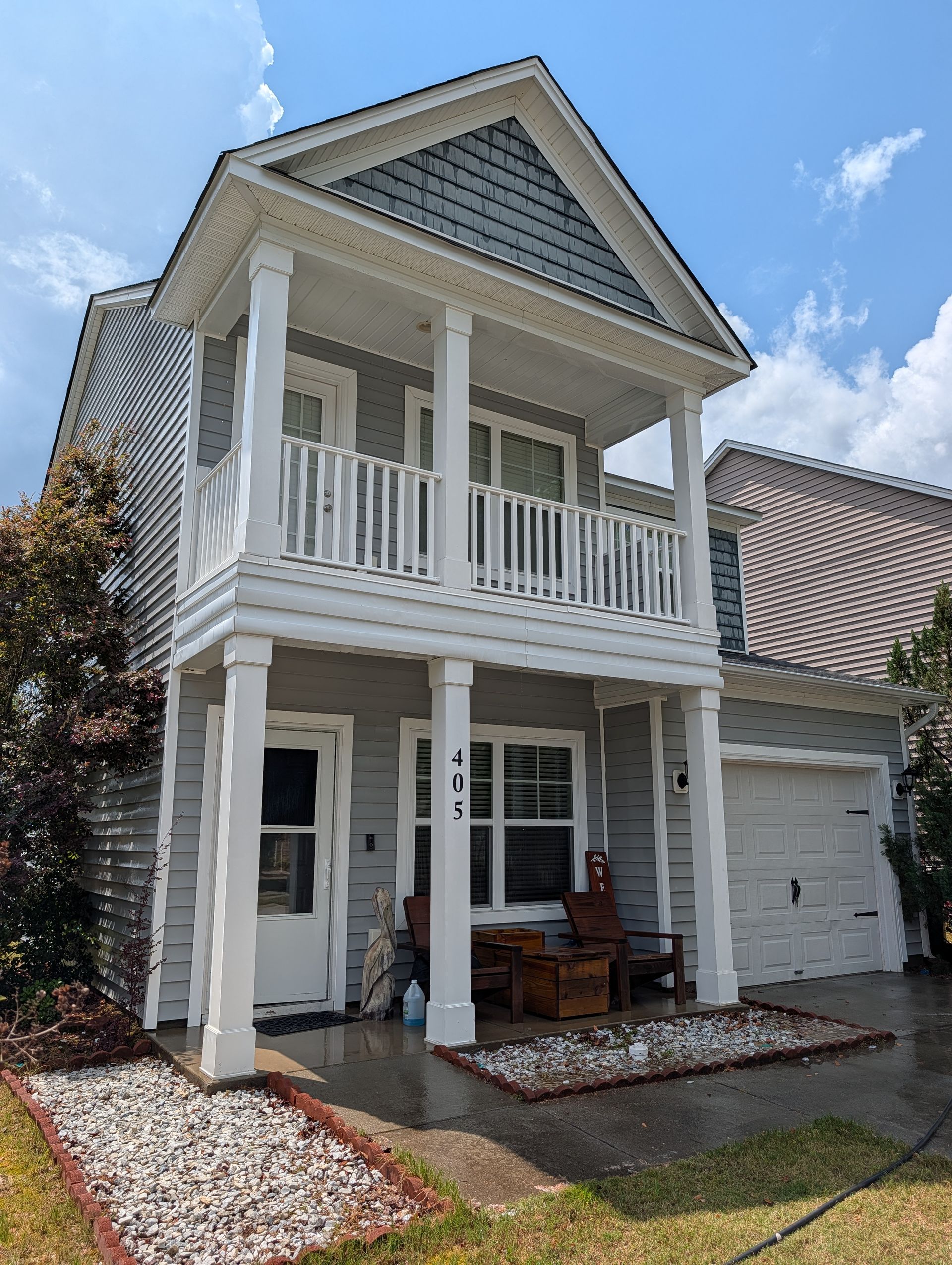 Two-story gray house with white trim, front porch, and balcony under a blue sky