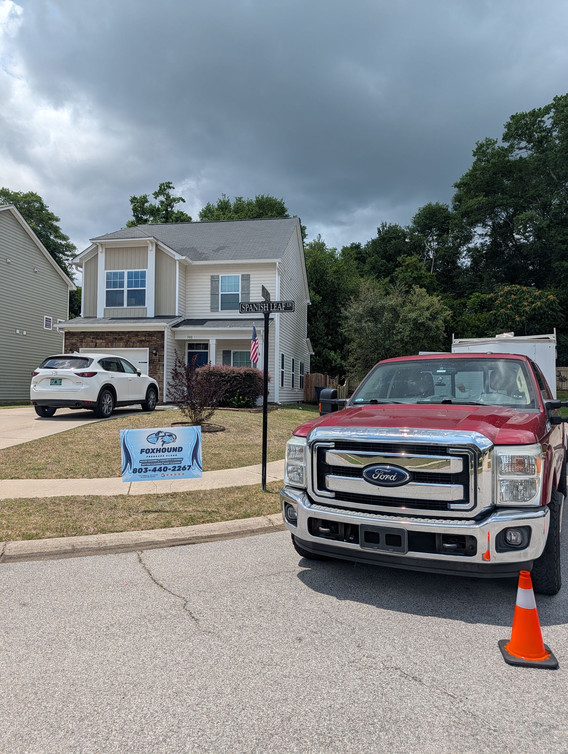 Suburban house under cloudy sky with red truck and orange cone in the driveway, and a white SUV nearby