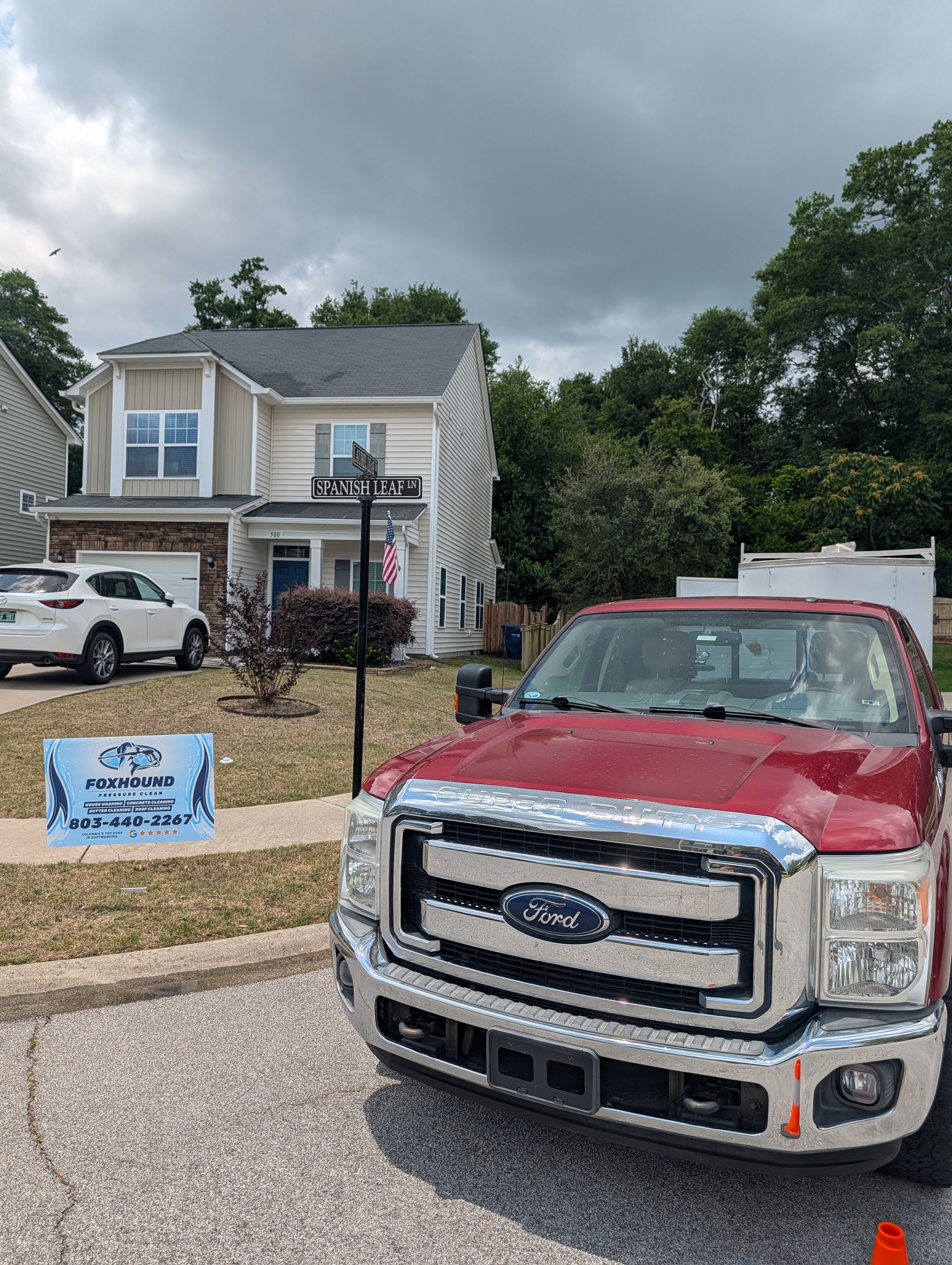 Red Ford pickup parked in front of a house with a real estate sign under cloudy skies