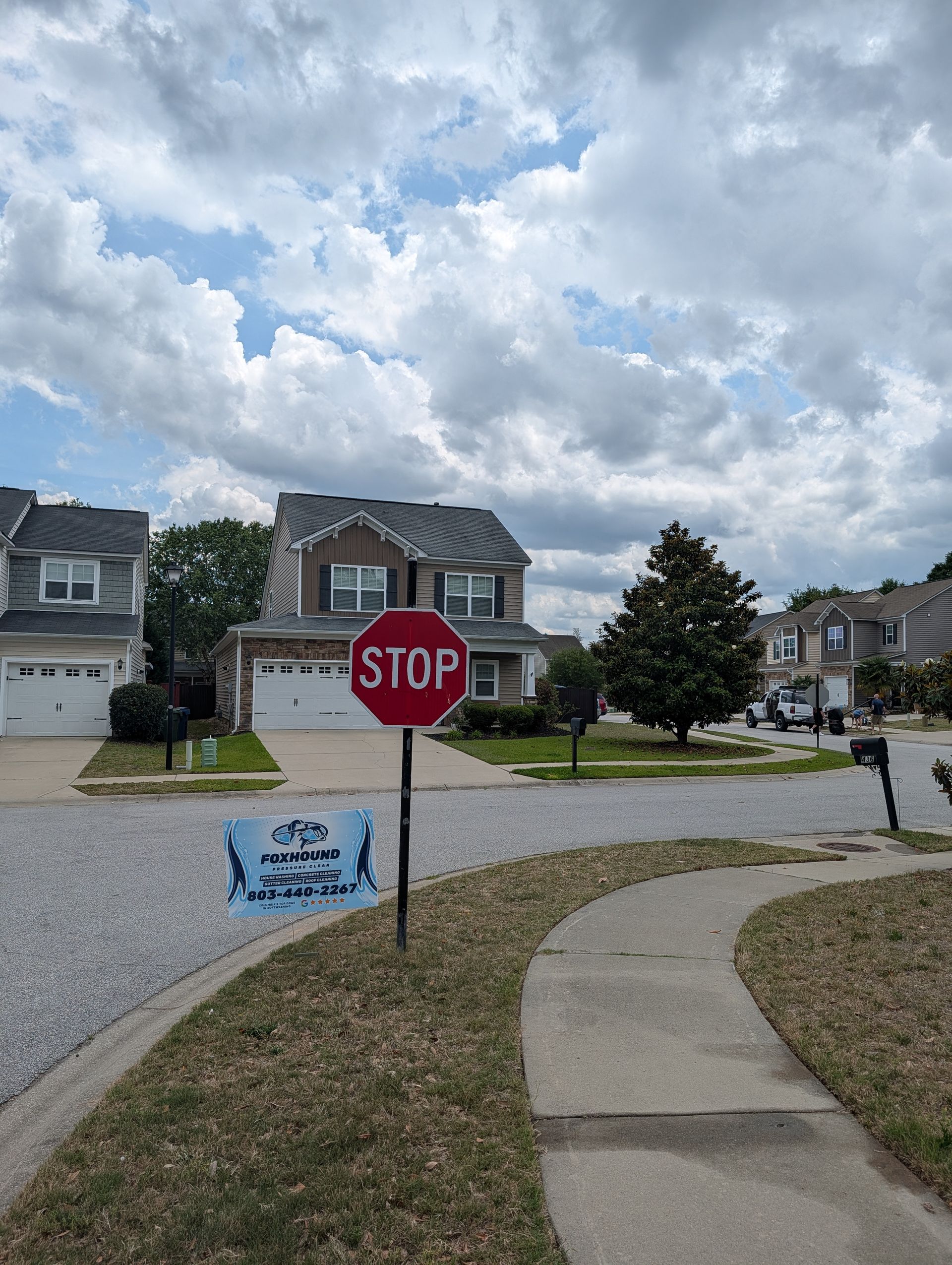 Suburban street with stop sign, sidewalk, gravel driveways, and cloudy sky.