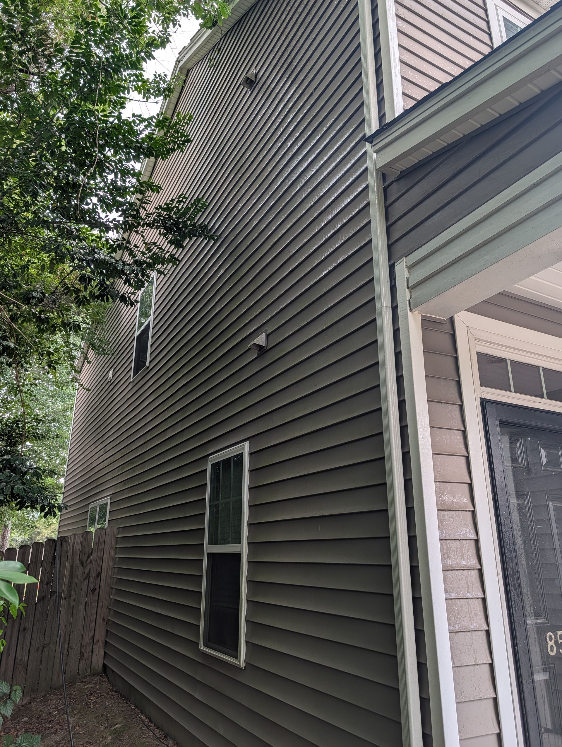 Side of a house with gray siding, two windows, and a tree-lined narrow yard.