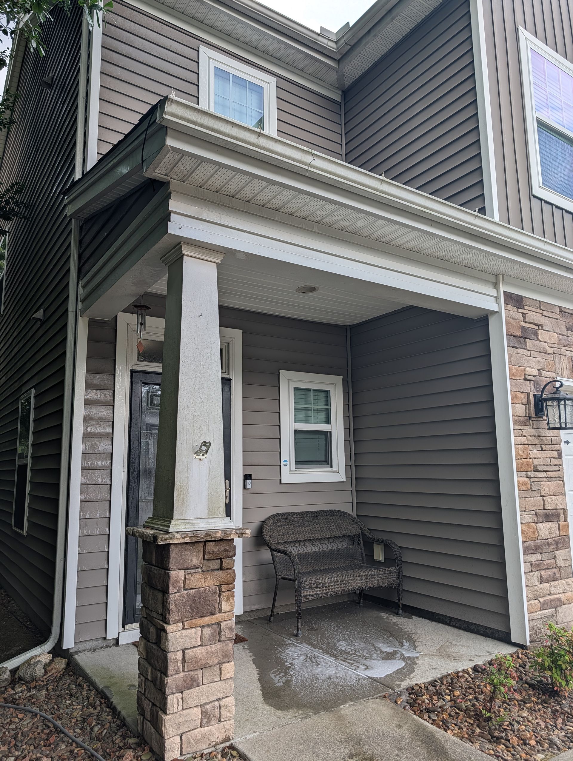 Front porch of a gray townhouse with white columns, a bench, and stone trim under the overhang
