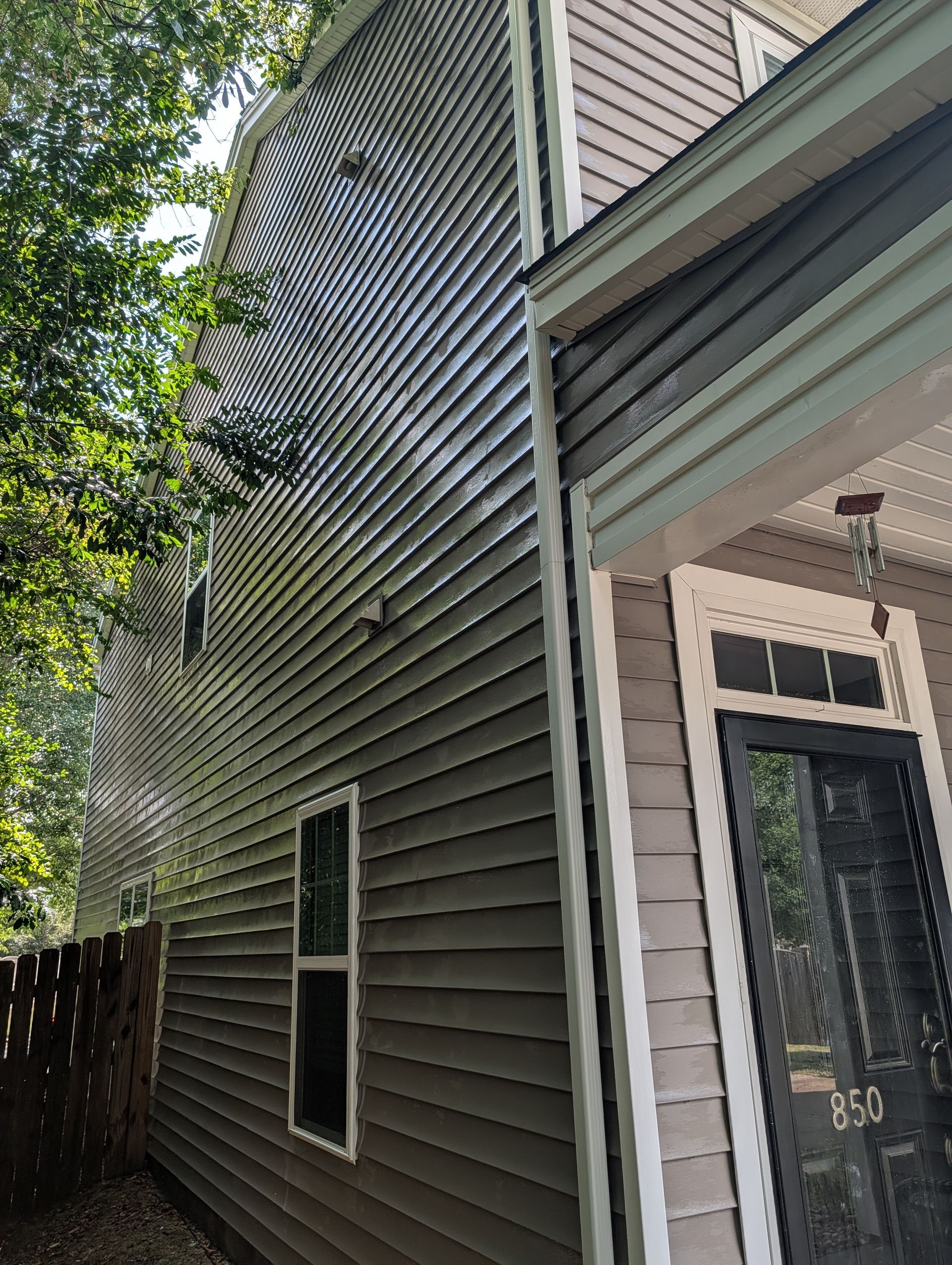 Side view of a gray house with white trim, windows, and a dark front door under tree shade.