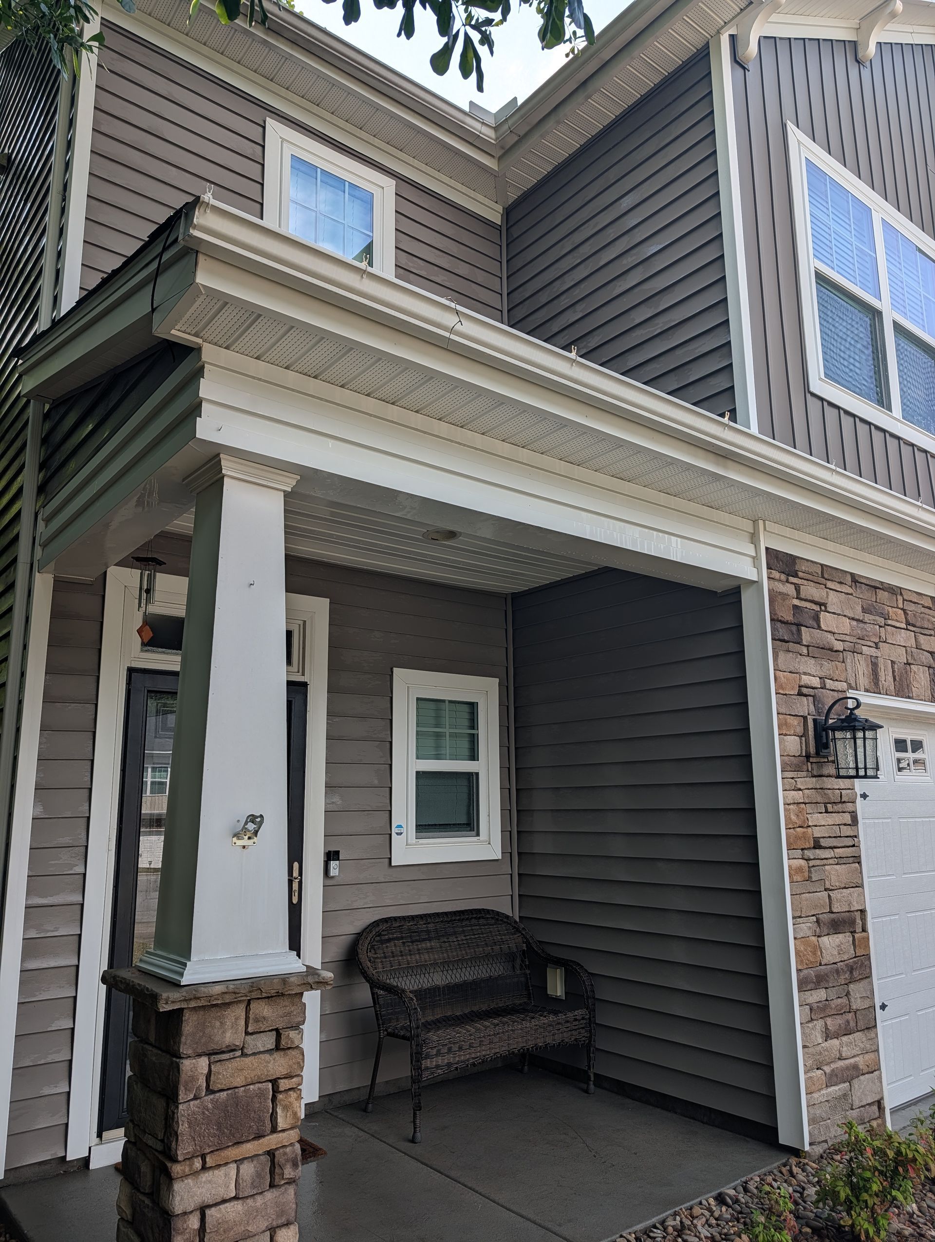 Front porch of a dark gray house with stone columns, a bench, and a small window under the eaves