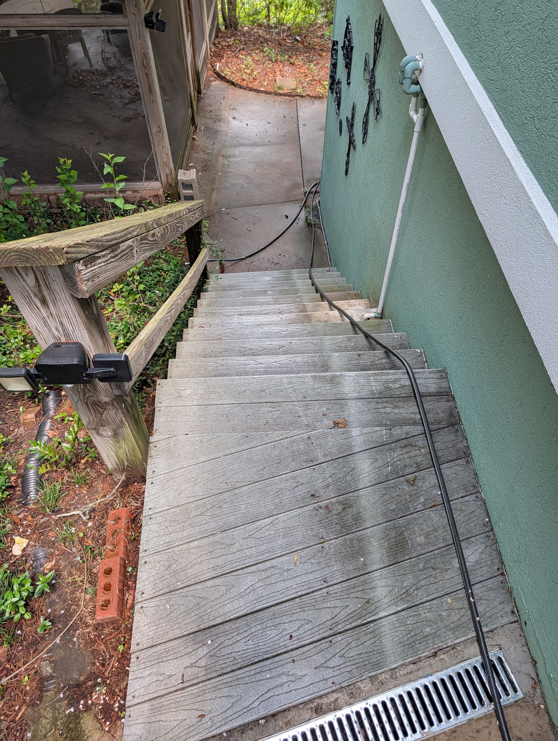 Steep concrete stairway with metal railing beside a green house, leading to a wet lower walkway.