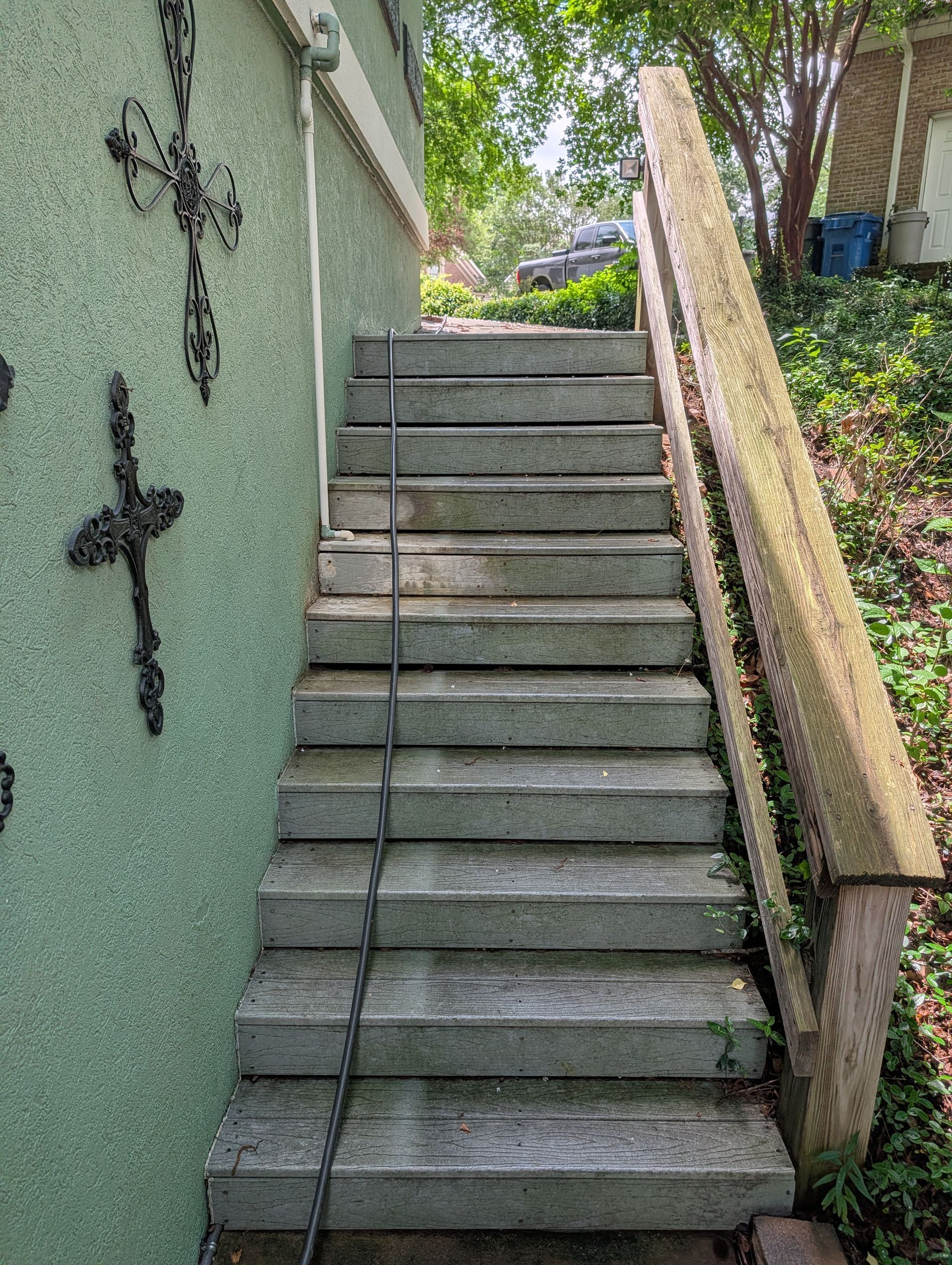 Steep outdoor concrete stairs beside a green stucco wall with black crosses and a wooden handrail