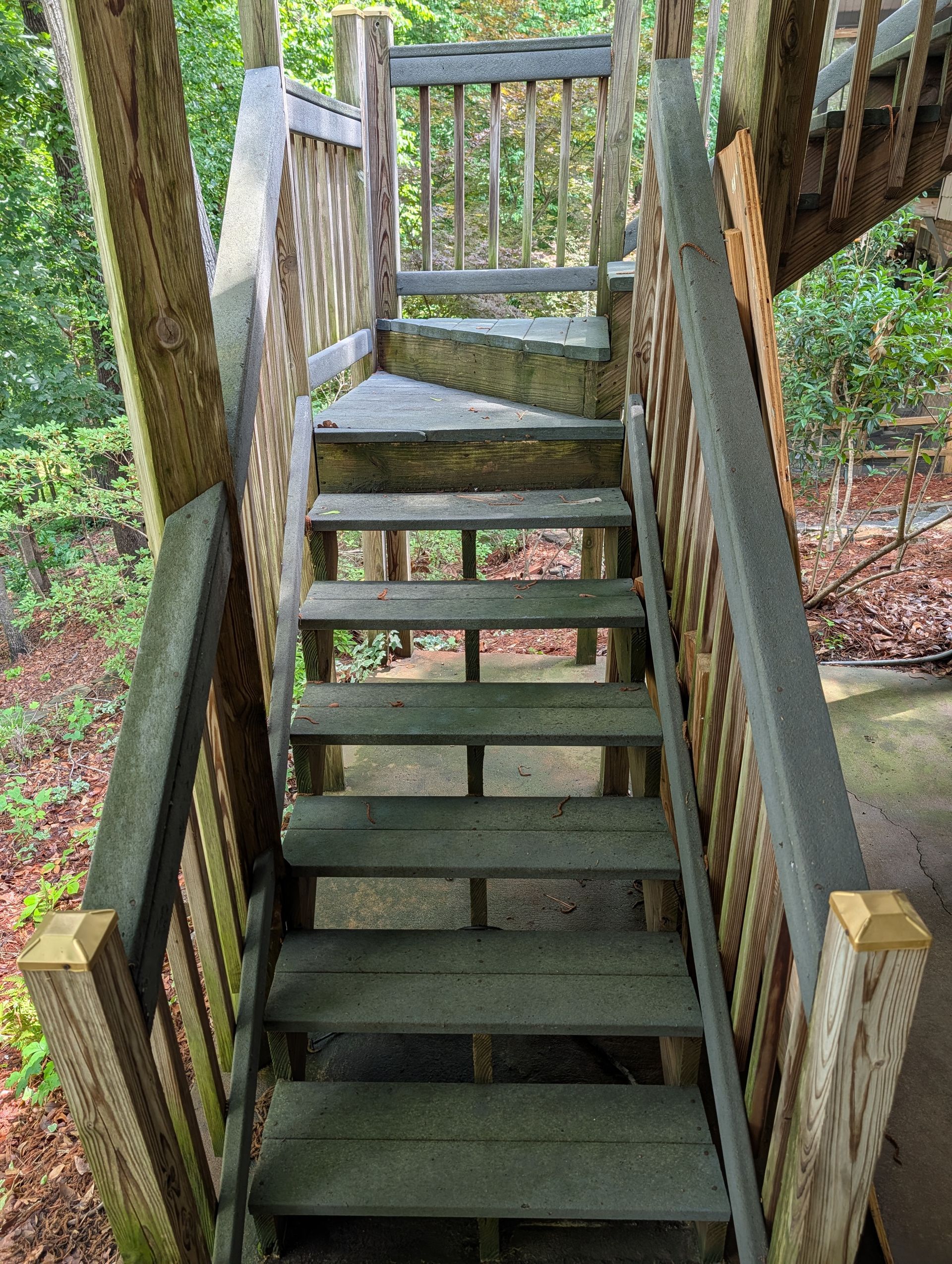 Wooden outdoor staircase with a slanted ramp, surrounded by trees and greenery.
