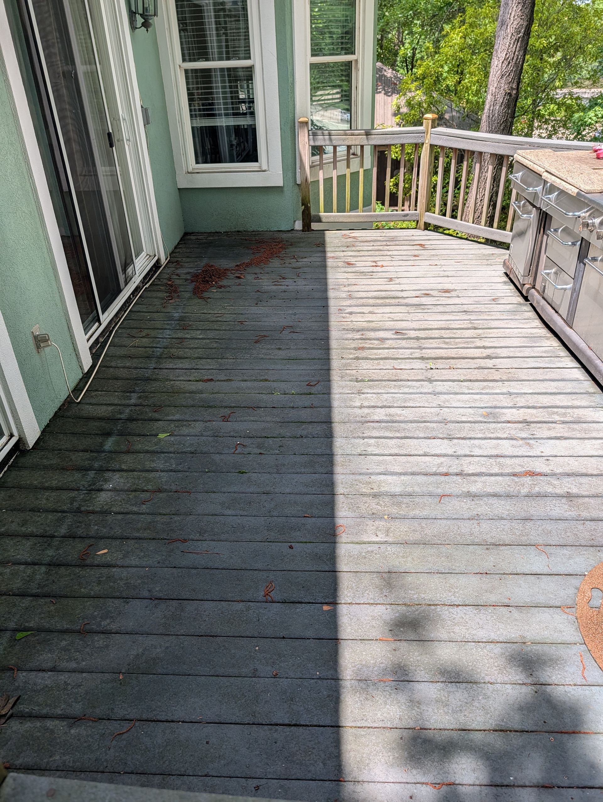 Weathered wooden porch deck beside a mint-green house, split between shade and sunlight.