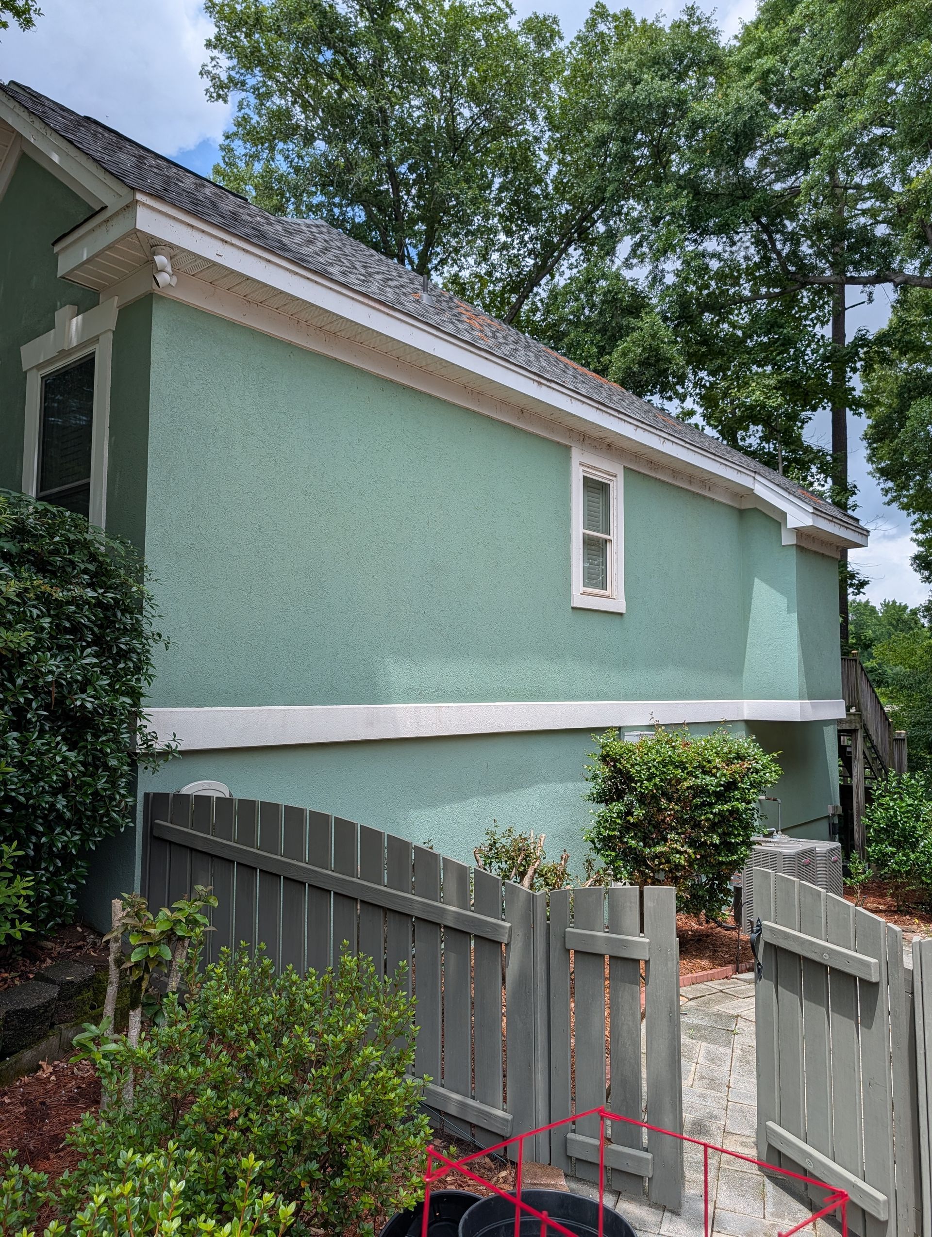 Green house exterior with white trim and a gray fence along a leafy yard