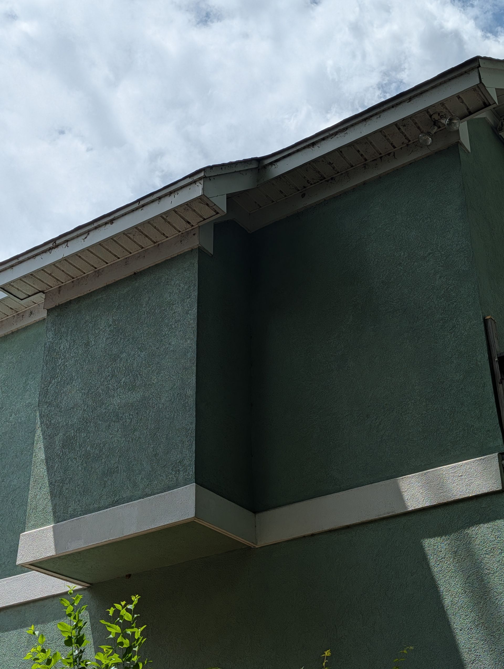 Green stucco house exterior with white trim and roofline against a cloudy sky